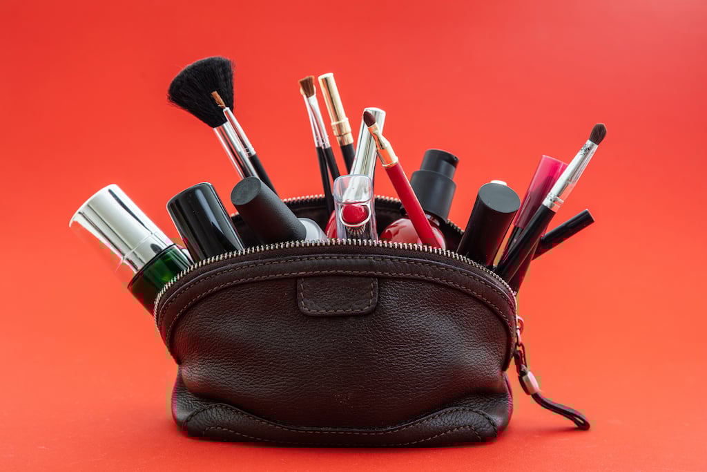 Makeup bag with cosmetics and makeup accessories against red background