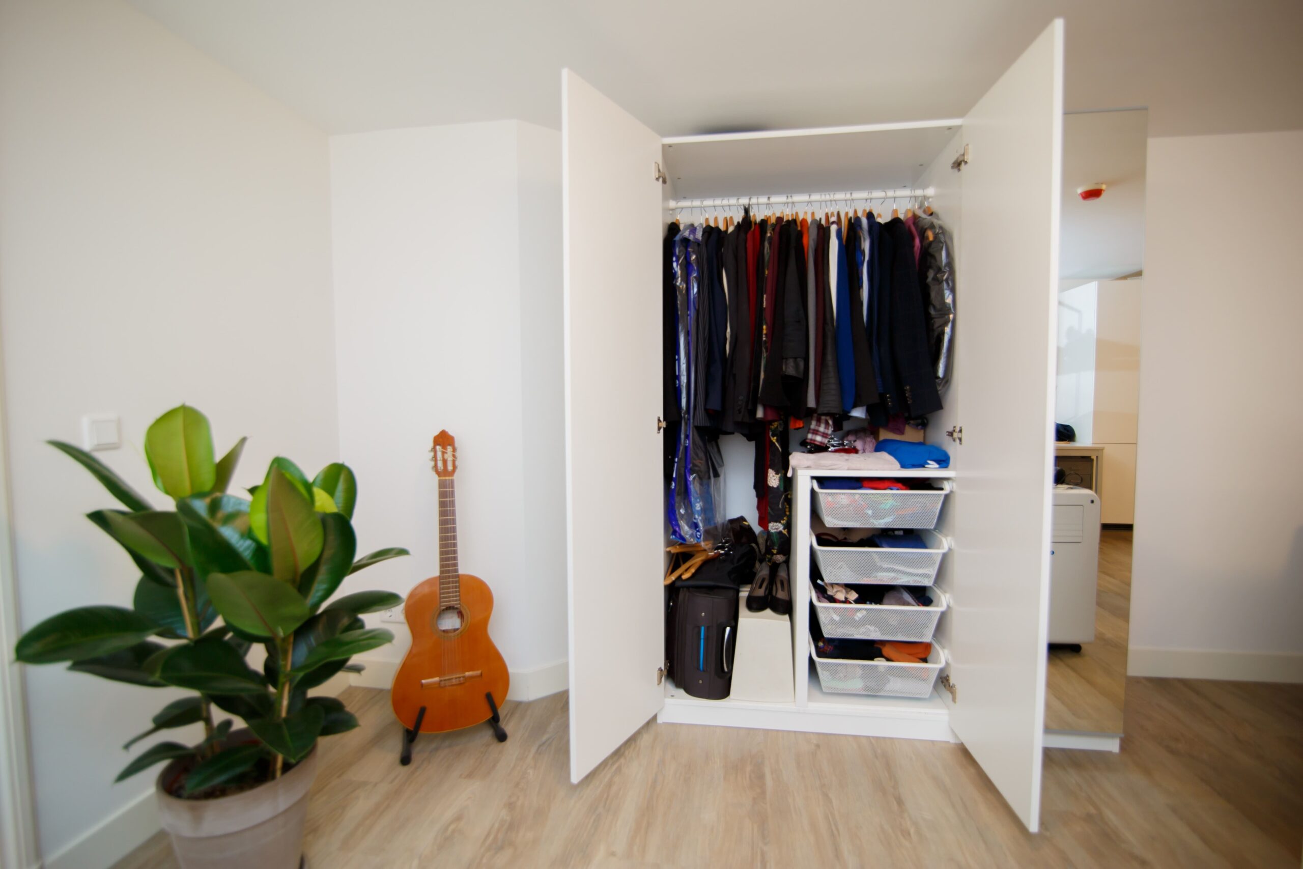 Bedroom with a full clothes closet , a guitar on the corner and a big green decoration plant 